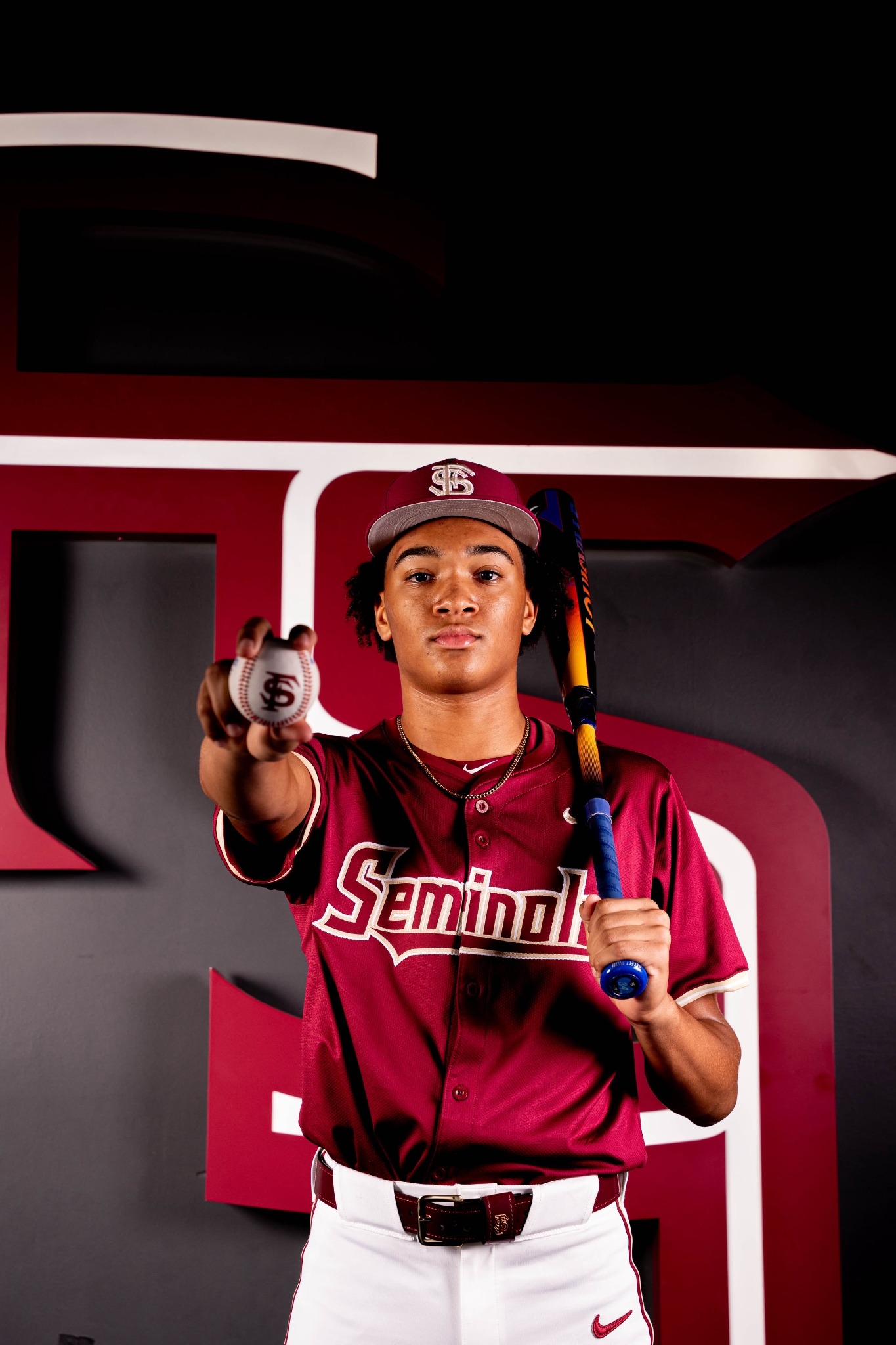 Devin Raines wearing a Florida State baseball uniform and holding a baseball and bat